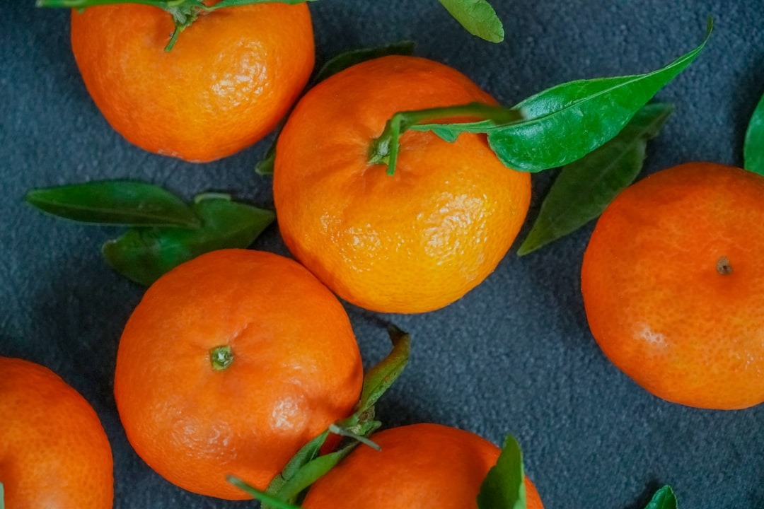 Fresh orange clementines with green leaves on a dark surface.
