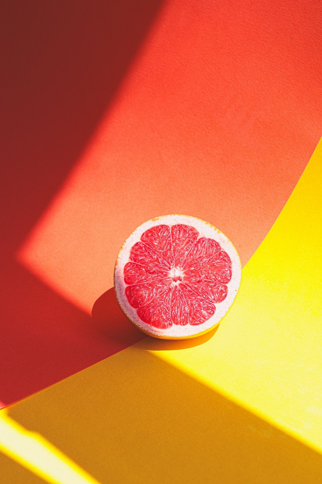 A sliced red grapefruit sits on a divided paper background.