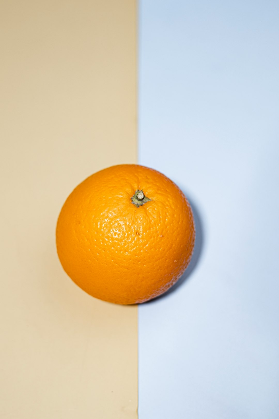 A whole orange sits on a background split between two colors.